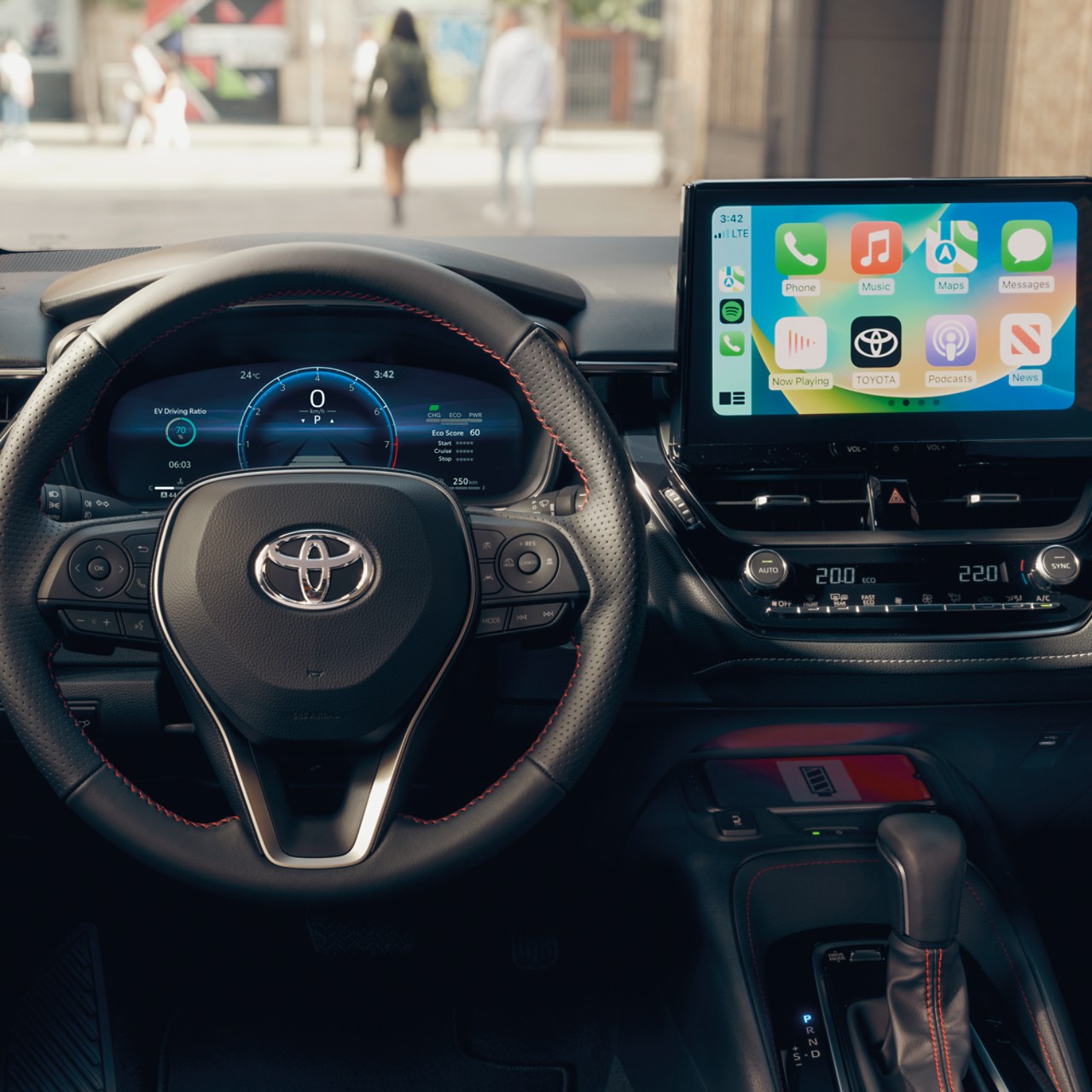 Na dotykovém displeji multimédií je vidět domovská obrazovka Apple CarPlay v kabině vozu Toyota s černou přístrojovou deskou.