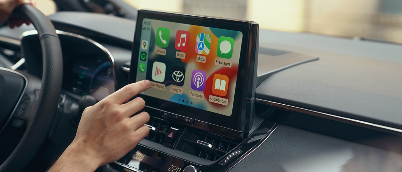 Osoba sedící v Toyotě používá dotykovou obrazovku palubních multimédií. Na displeji se zobrazuje domovská obrazovka Apple CarPlay.